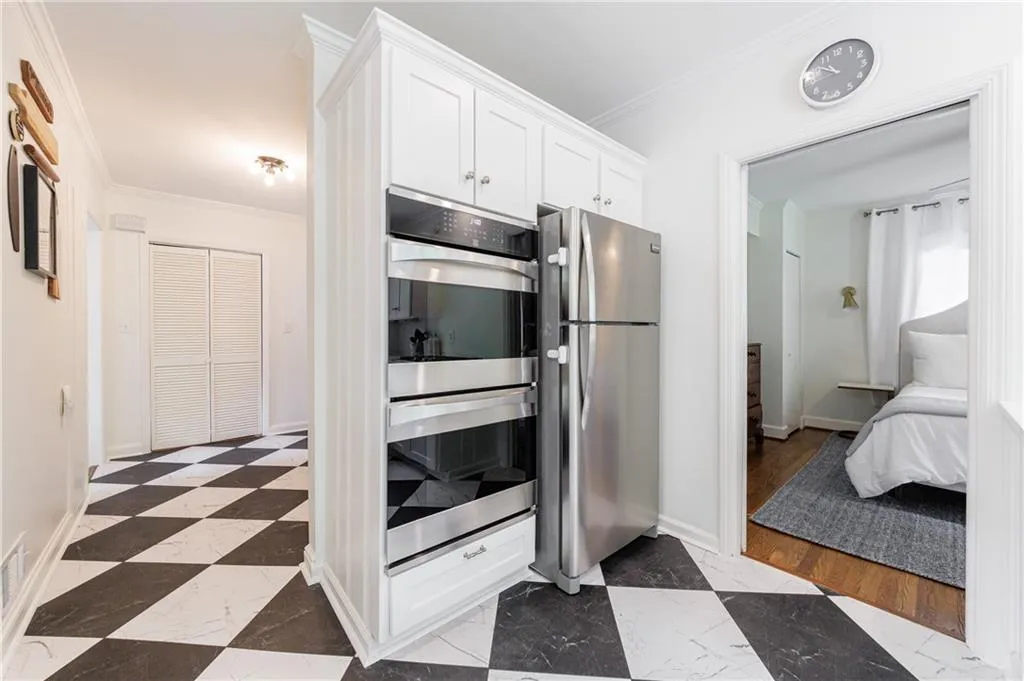 Kitchen featuring stainless steel appliances, crown molding, white cabinetry, dark marble finish floors, and baseboards