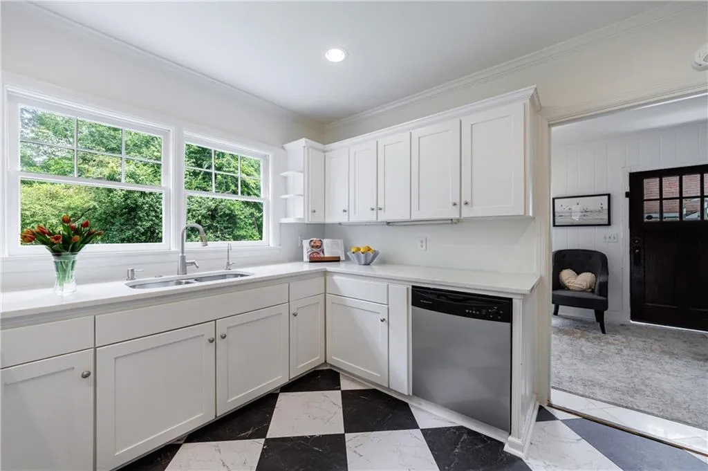 Kitchen with stainless steel dishwasher, a sink, dark marble finish floors, ornamental molding, and light countertops