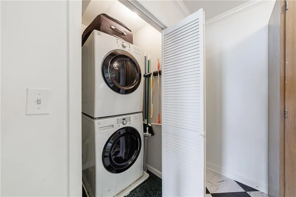 Laundry area with stacked washer and clothes dryer, baseboards, marble finish flooring, and ornamental molding