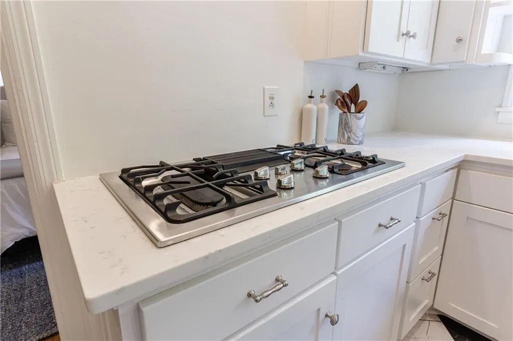 Kitchen view of stainless steel gas stovetop, white cabinetry, and light stone counters