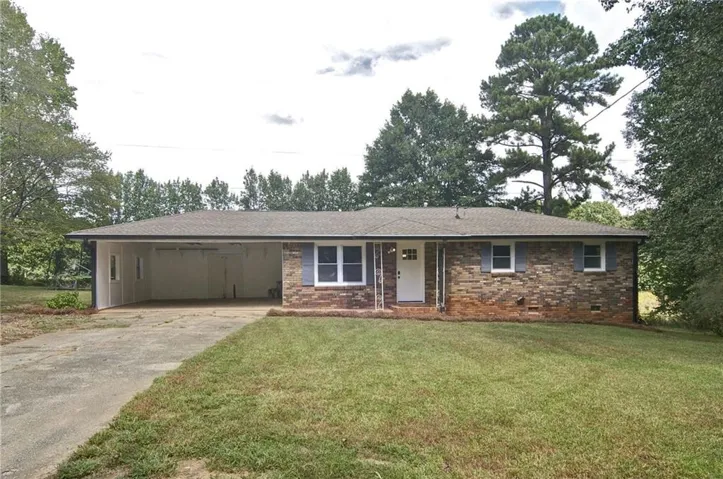 Brick exterior with a covered carport, front entry door, and a grass lawn