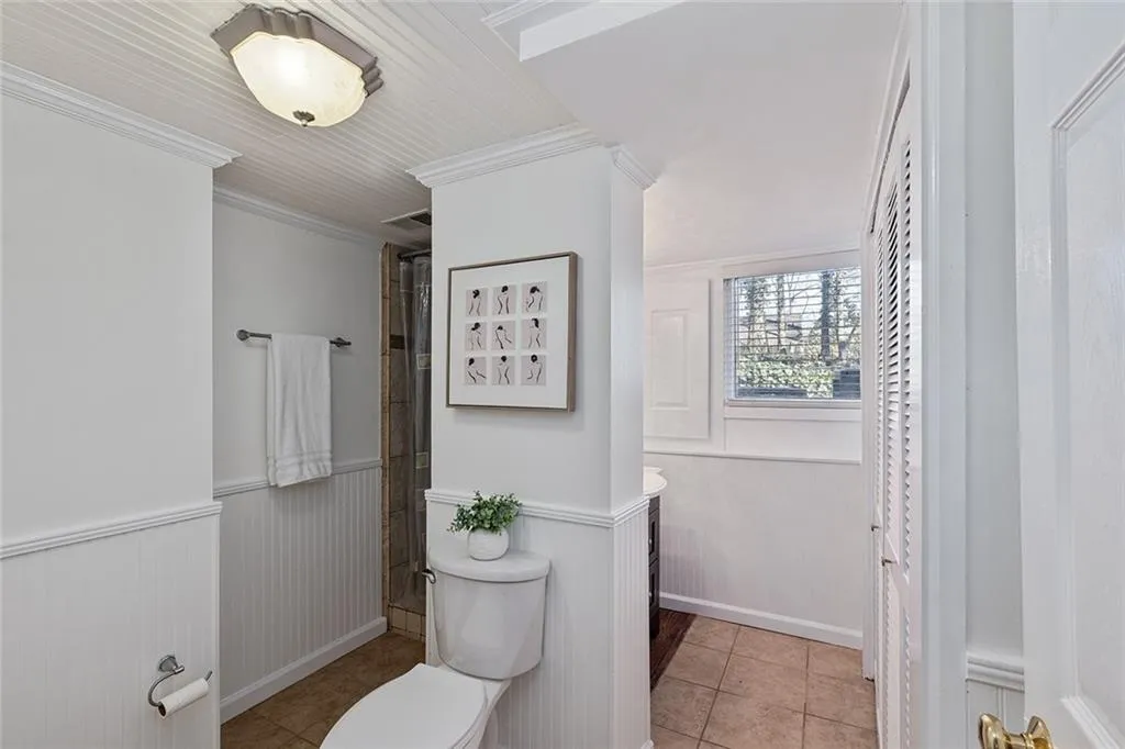 Bathroom featuring ornamental molding, vanity, light tile patterned floors, a wainscoted wall, and a shower