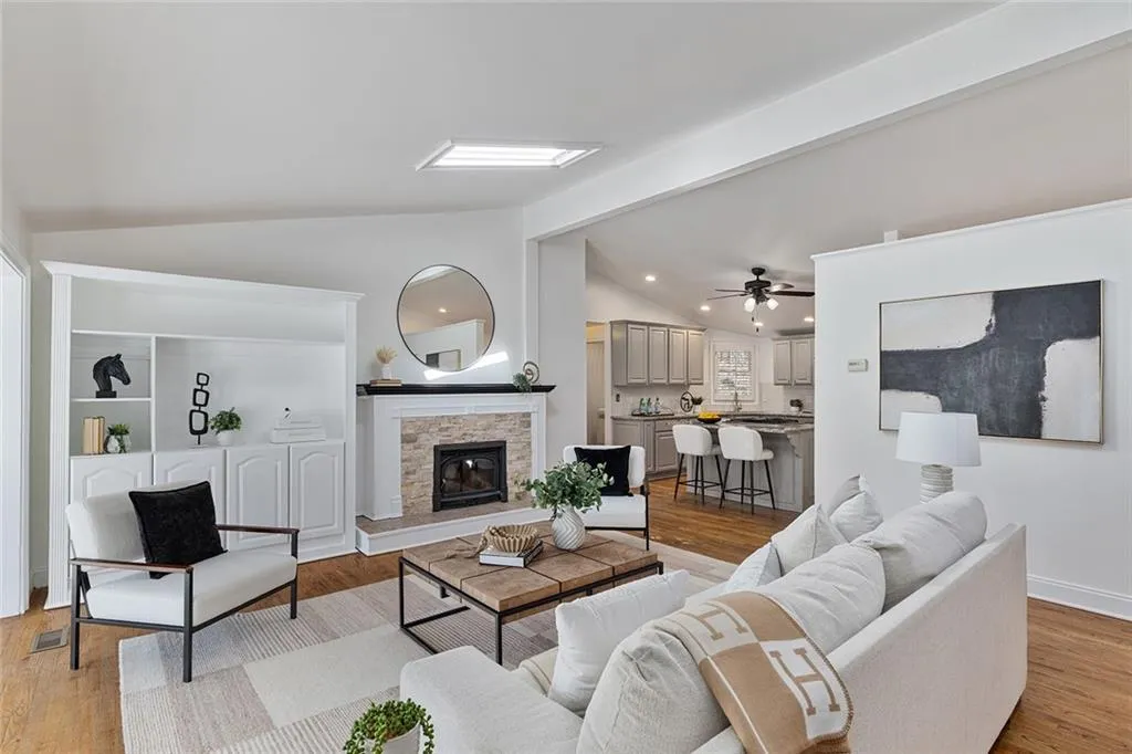 Living room featuring light wood-style flooring, lofted ceiling, a fireplace, and a ceiling fan
