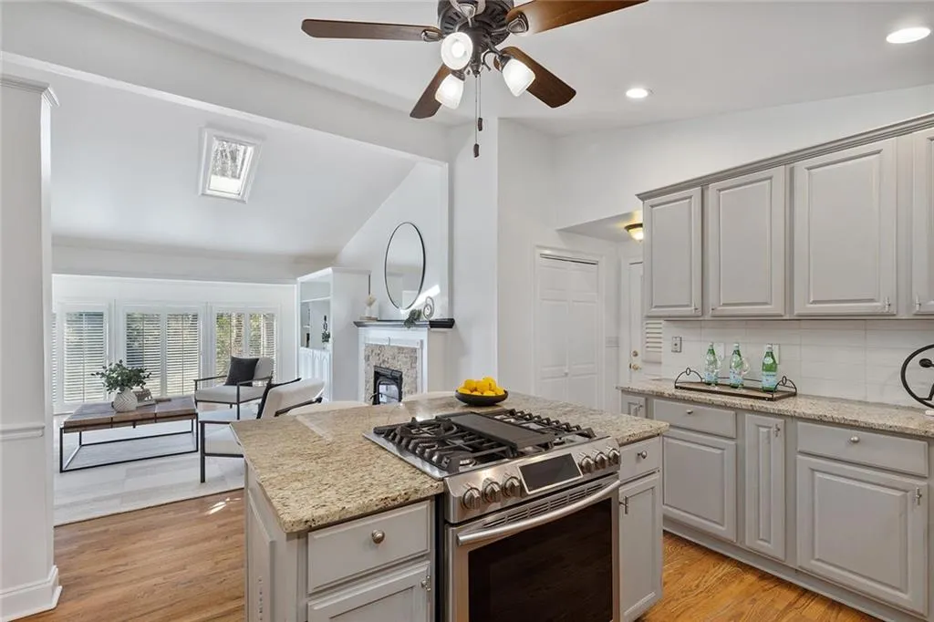 Kitchen with stainless steel range with gas stovetop, light stone countertops, vaulted ceiling, tasteful backsplash, and light wood-type flooring