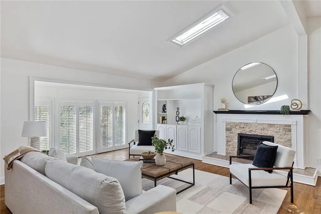 Living area with wood finished floors, lofted ceiling, a fireplace, and a skylight