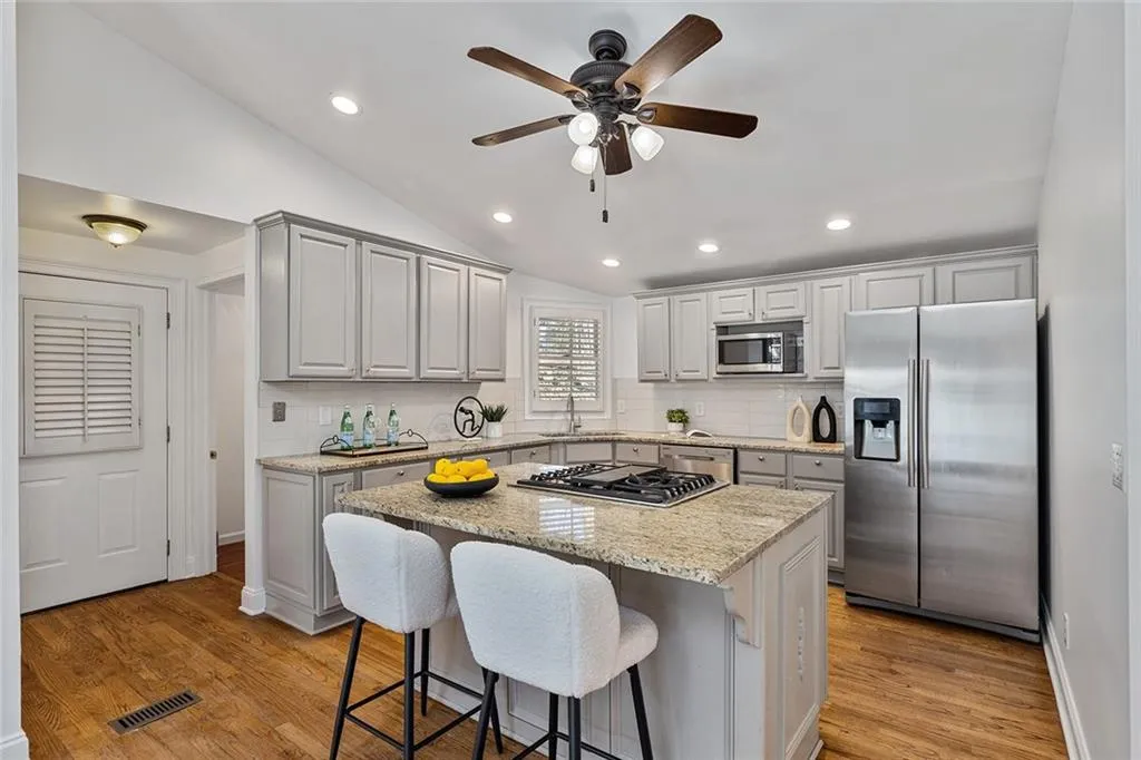 Kitchen with lofted ceiling, stainless steel appliances, light stone counters, a ceiling fan, and a center island