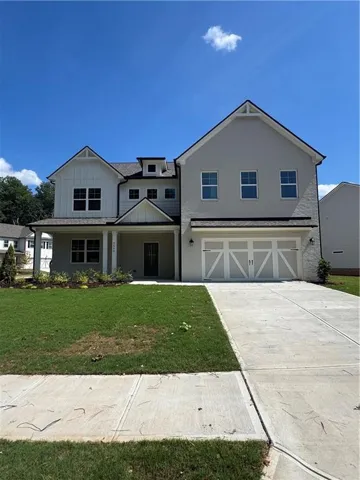 Two-story residence featuring a light-colored exterior with dark trim accents, a large two-car garage with decorative doors, a covered front porch, and a well-maintained lawn