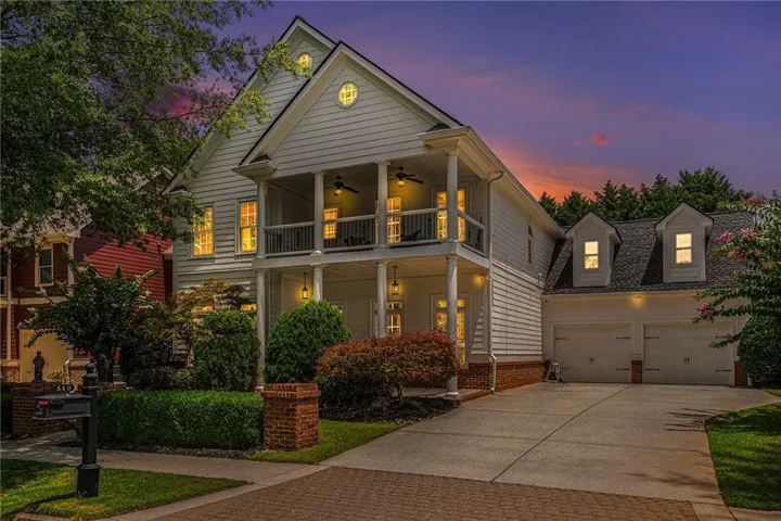 Two-story residence featuring a covered front porch, upper-level balcony, two front-facing dormer windows, and an attached two-car garage