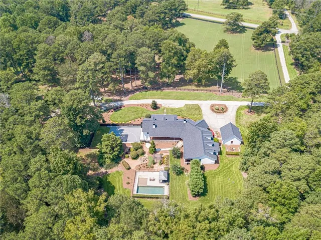Expansive estate featuring a large main residence, detached auxiliary building, swimming pool with surrounding patio, circular driveway, and mature landscaping