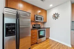 Kitchen with stainless steel appliances, brown cabinets, dark countertops, decorative backsplash, and light wood-type flooring