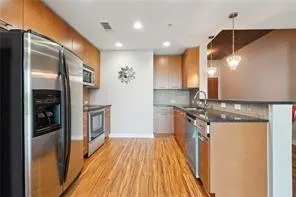 Kitchen with stainless steel appliances, decorative backsplash, dark countertops, light wood-style flooring, and a peninsula