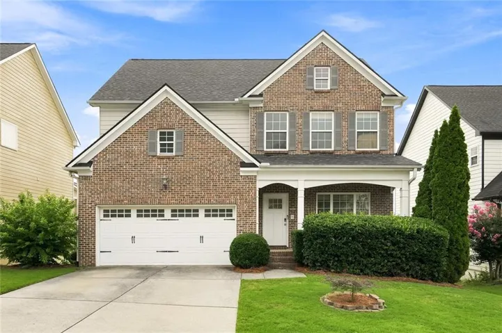 Traditional brick and siding exterior featuring a covered front entry, an attached two-car garage with carriage-style doors, and mature landscaping