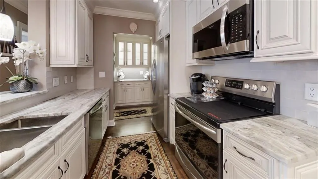 Kitchen featuring stainless steel appliances, white cabinetry, ornamental molding, decorative backsplash, and light stone countertops