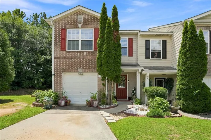 Two-story townhome featuring a brick facade with red shutters, a concrete driveway, and a covered entryway