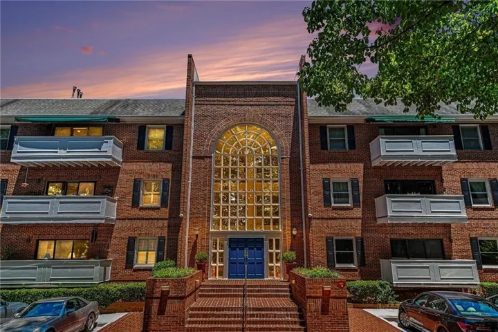 Brick-clad multi-story building featuring a prominent arched window facade, multiple private balconies, and a deep blue double-door entrance