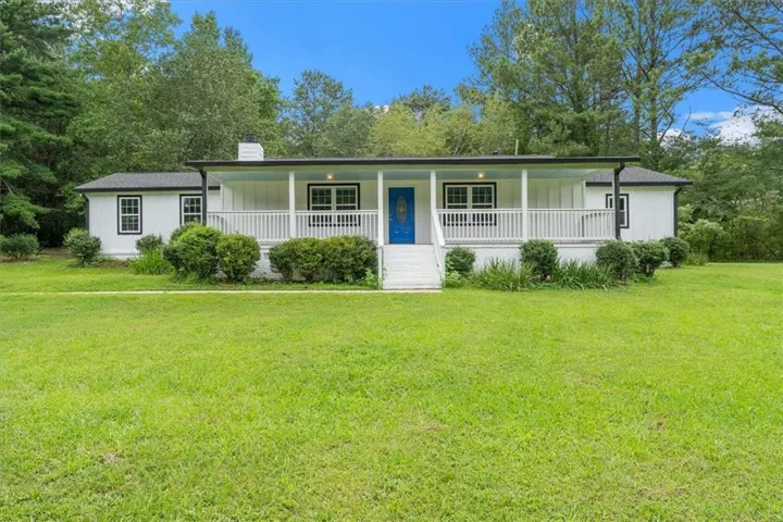 Ranch-style residence featuring a white exterior with black trim windows, a covered front porch with white railings, and a prominent blue entry door