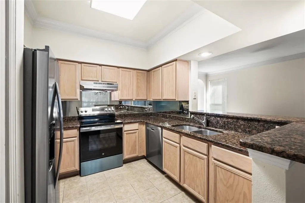 Kitchen with ornamental molding, light brown cabinets, appliances with stainless steel finishes, dark stone countertops, and light tile patterned floors