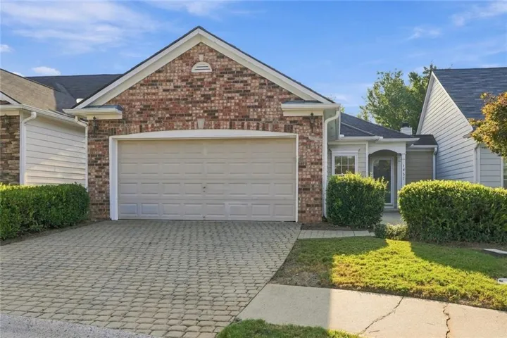 Brick and siding exterior with an attached garage, paver driveway, and mature shrubbery