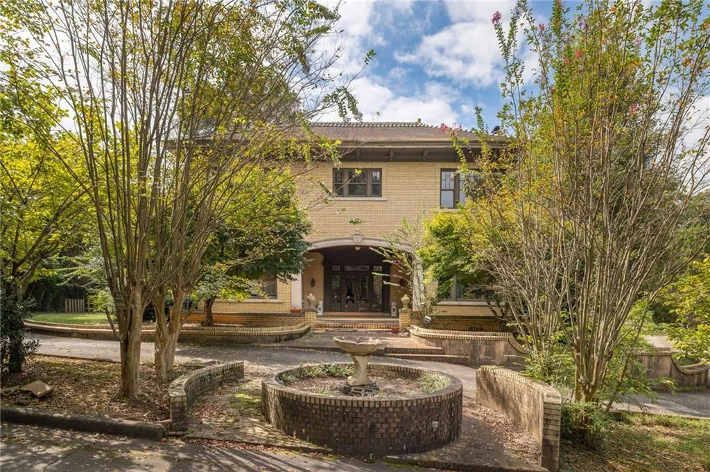 Brick exterior with a prominent arched entry, mature trees, and a decorative fountain feature