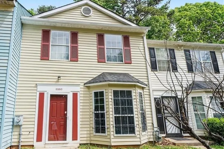 Two-story townhouse with a red paneled front door, bay window, and red louvered shutters