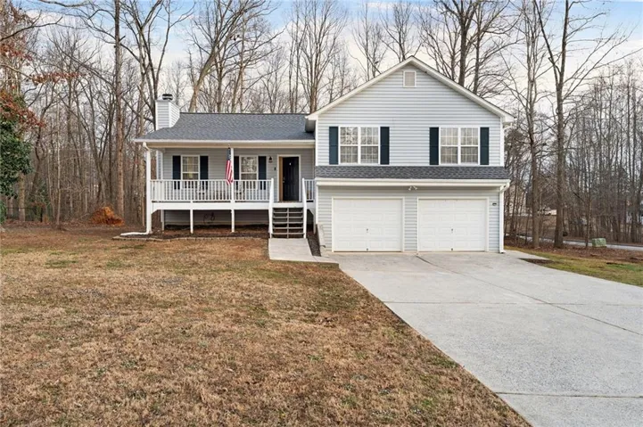Split level home featuring a porch, an attached garage, driveway, a front lawn, and a chimney