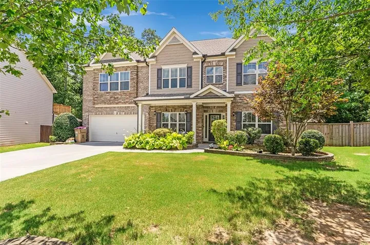 Two-story residence featuring a brick and siding facade, a covered front entry, an attached two-car garage, mature landscaping, and a fenced rear yard