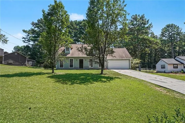 Light green exterior with a two-car garage, dormer windows, and a paved driveway