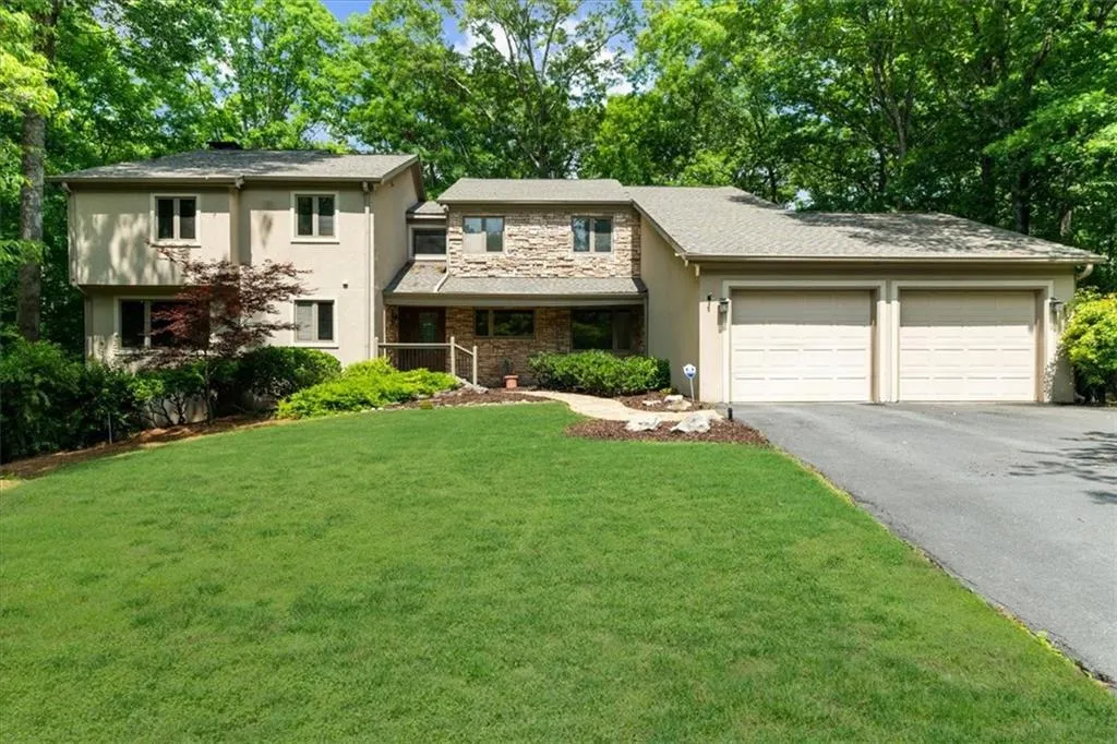 View of front of property featuring an attached garage, asphalt driveway, stucco siding, a front yard, and stone siding