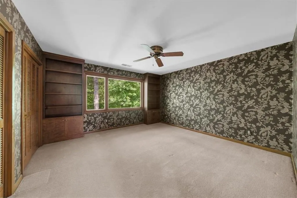 Spare room featuring wallpapered walls, ceiling fan, carpet flooring, and baseboards