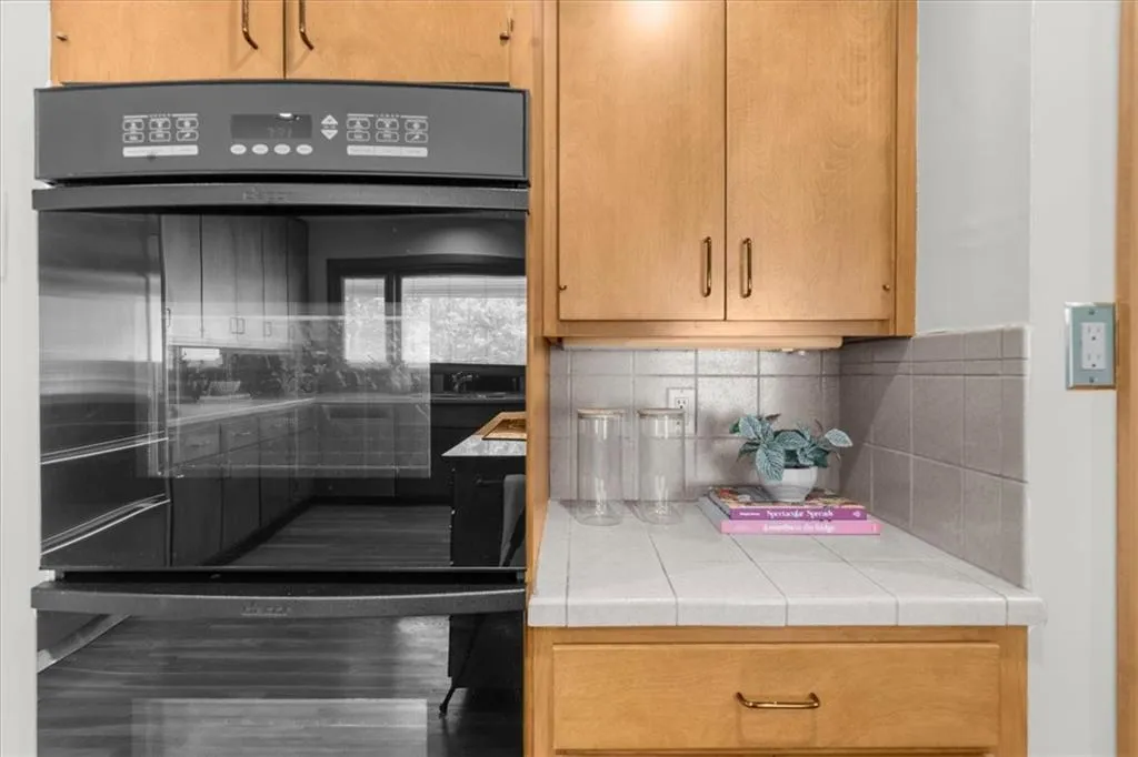 Kitchen featuring tile countertops, decorative backsplash, and wood finished floors