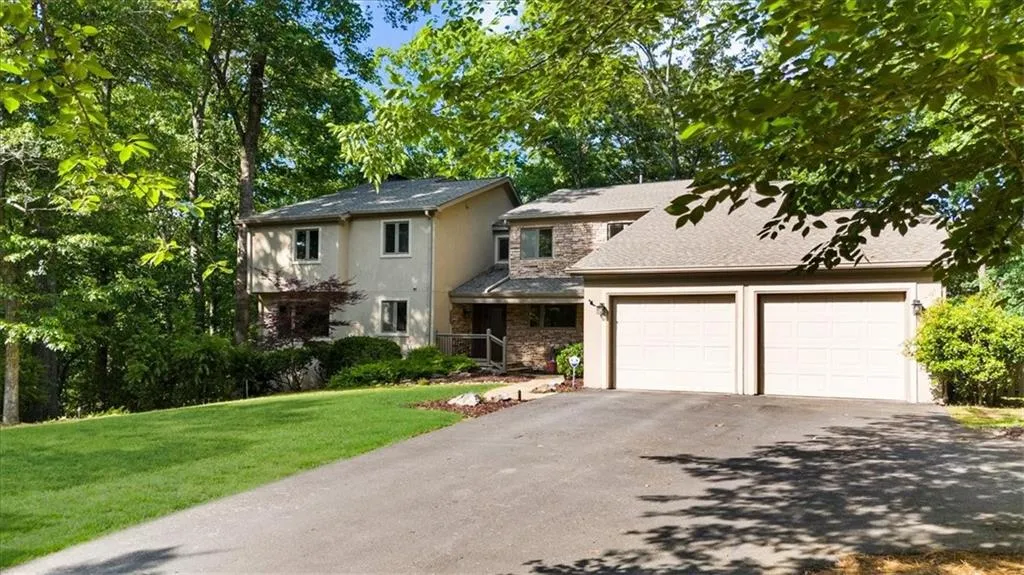 View of front of house featuring asphalt driveway, an attached garage, stucco siding, a front yard, and stone siding
