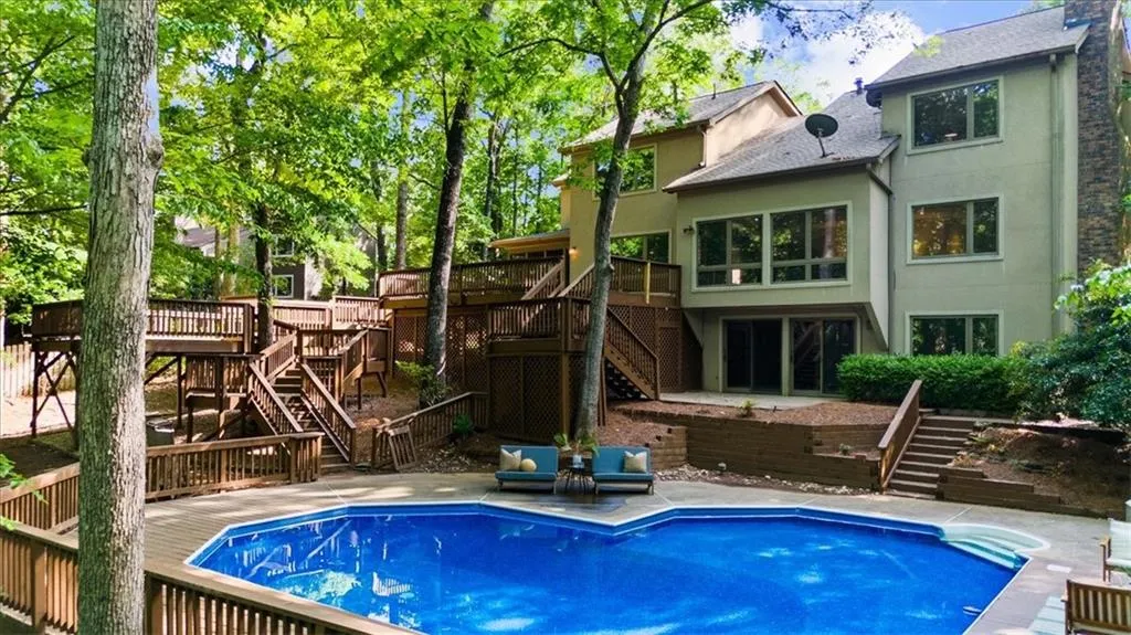 Rear view of property with stairs, a deck, stucco siding, and an outdoor pool