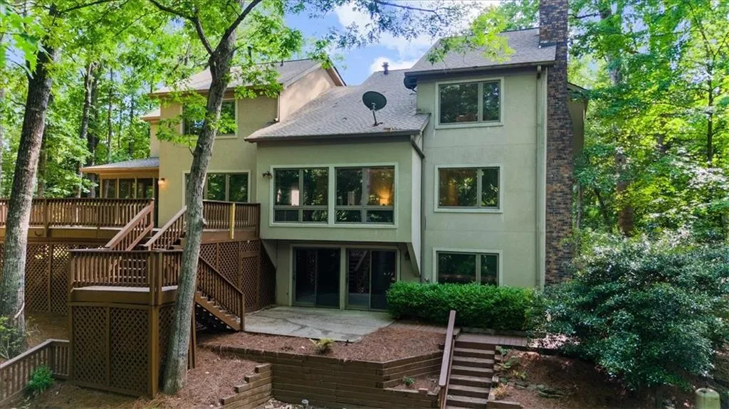Rear view of house featuring stairs, stucco siding, a deck, a chimney, and roof with shingles