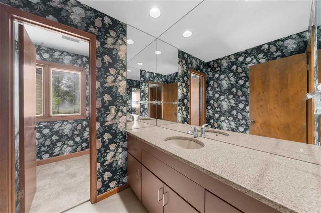 Bathroom with wallpapered walls, baseboards, recessed lighting, and vanity