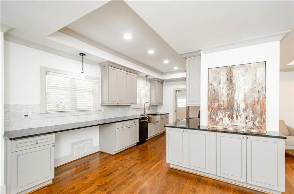 Kitchen with a tray ceiling, decorative light fixtures, dark wood-type flooring, backsplash, and dark stone countertops