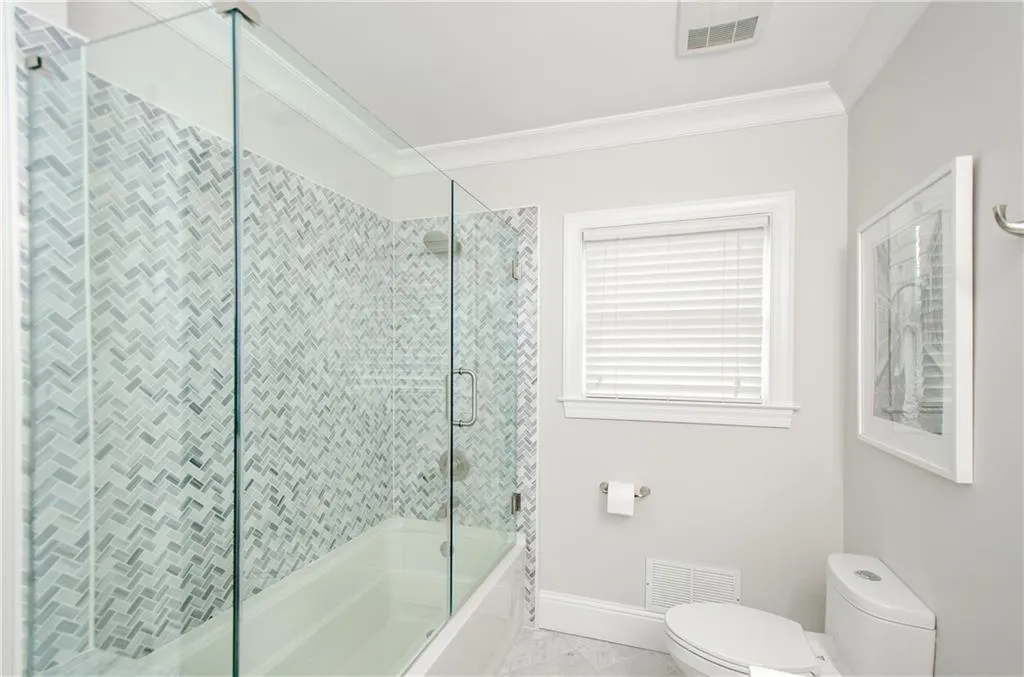 Bathroom featuring shower / bath combination with glass door, marble look tiles, and ornamental molding