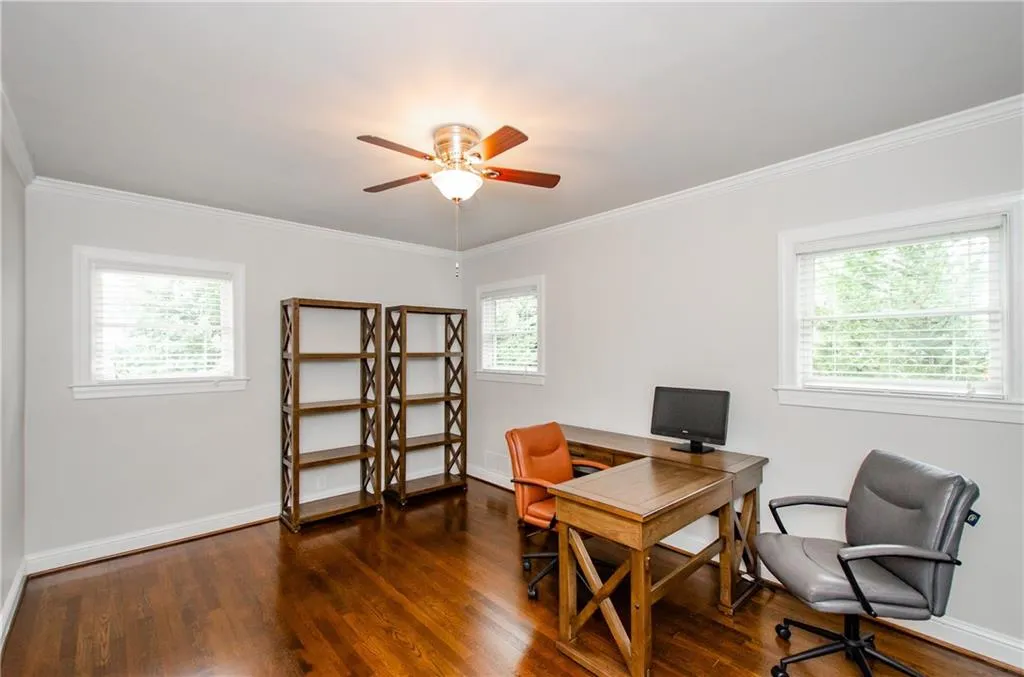 Office space featuring dark wood-type flooring, a ceiling fan, and ornamental molding