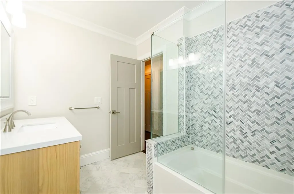 Bathroom featuring ornamental molding, vanity, bath / shower combo with glass door, and light marble finish floors