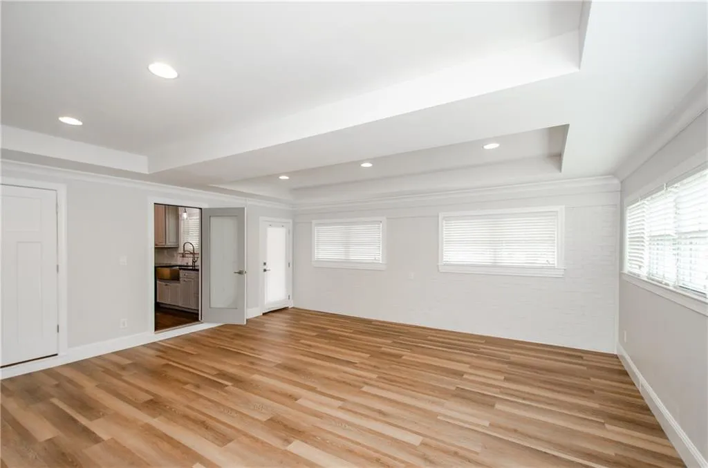 Unfurnished bedroom featuring a raised ceiling, brick wall, multiple windows, light wood-style flooring, and recessed lighting