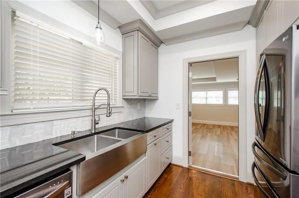 Kitchen with freestanding refrigerator, dark wood-style flooring, backsplash, dark stone counters, and gray cabinetry