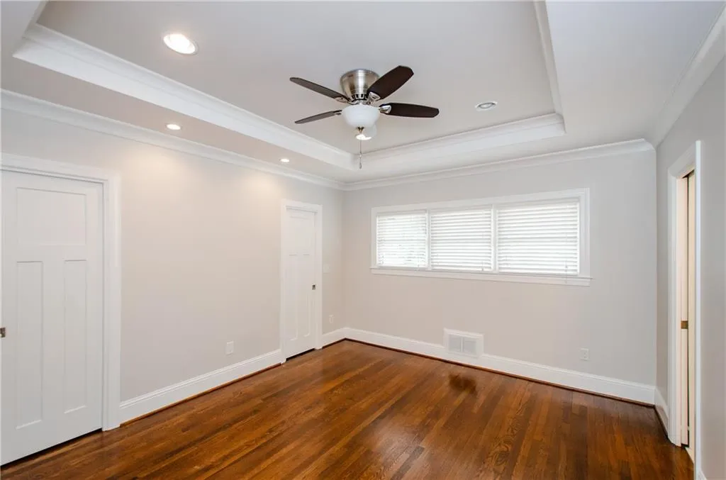 Unfurnished bedroom featuring dark wood-style flooring, ceiling fan, crown molding, a raised ceiling, and recessed lighting