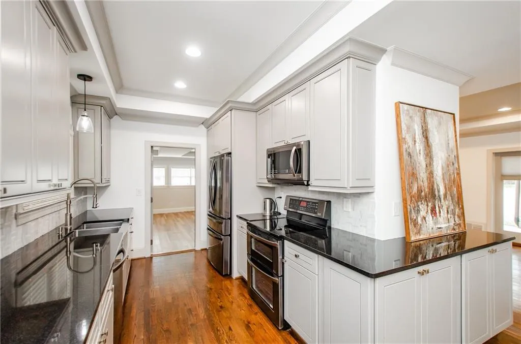 Kitchen with stainless steel appliances, tasteful backsplash, dark wood-style floors, dark stone countertops, and decorative light fixtures