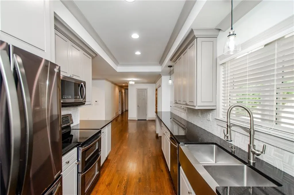 Kitchen featuring decorative light fixtures, stainless steel appliances, dark wood-type flooring, decorative backsplash, and a tray ceiling