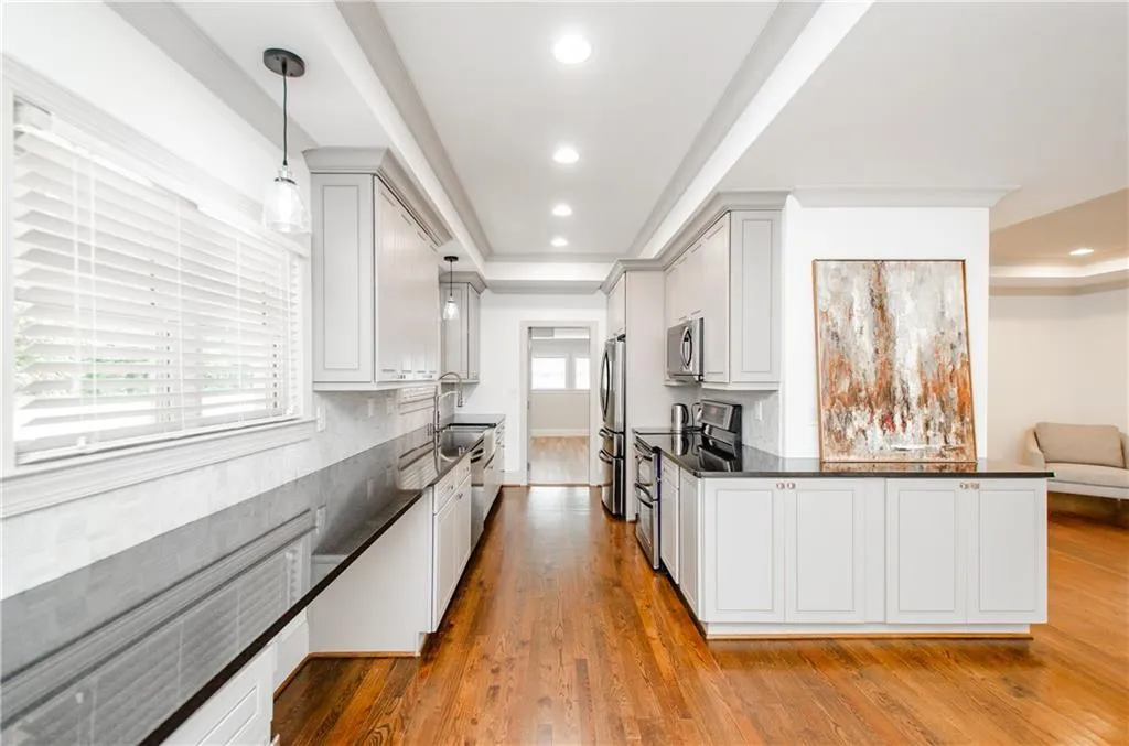 Kitchen featuring light wood-style flooring, decorative light fixtures, stainless steel appliances, dark stone counters, and a raised ceiling