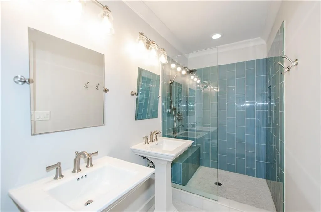 Full bathroom with a tile shower, two sinks, and crown molding