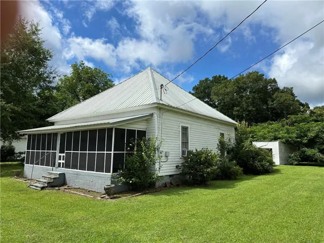 White siding exterior with a metal roof, screened porch, and mature landscaping