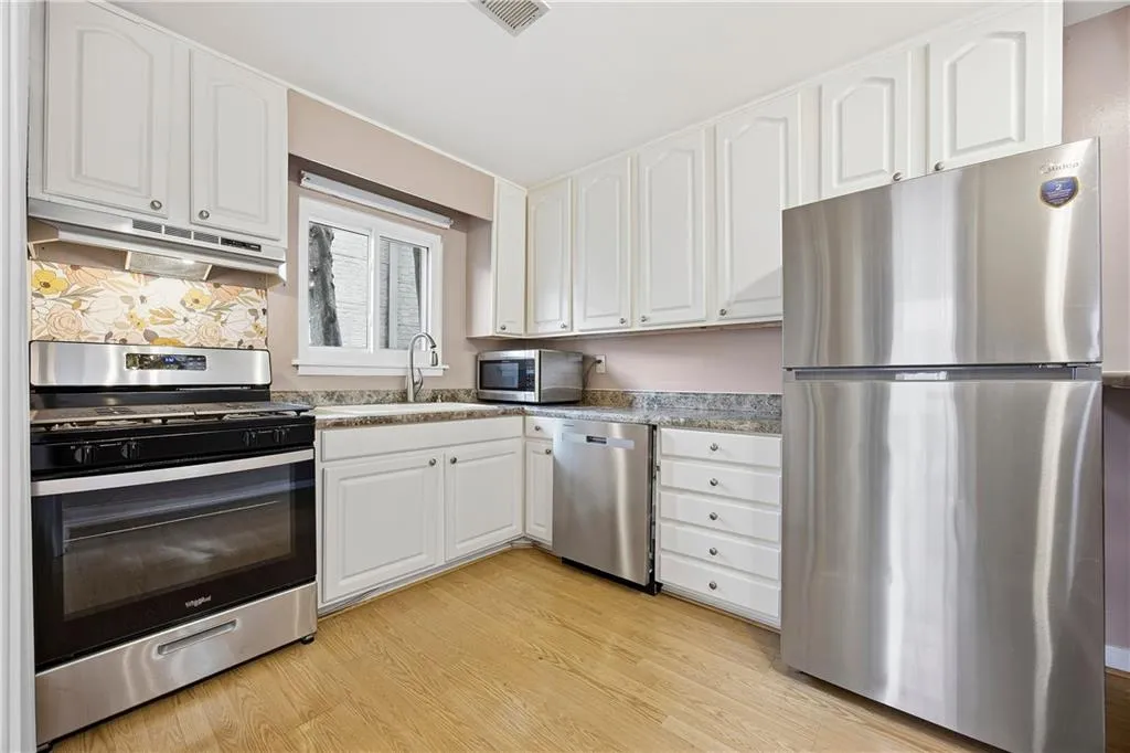Kitchen with brand new stainless steel appliances, white cabinetry, under cabinet range hood, light wood-style floors, and light countertops