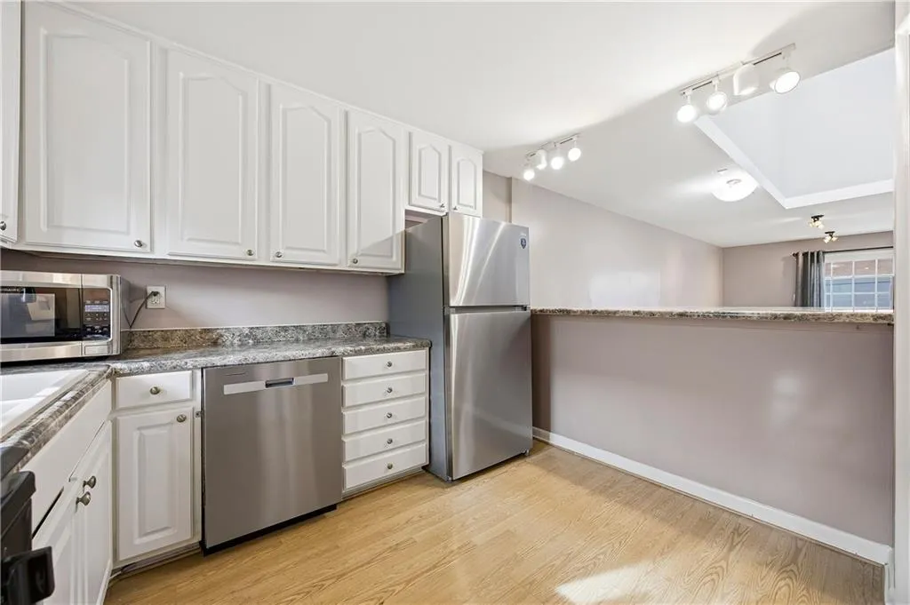 Kitchen featuring white cabinetry, appliances with stainless steel finishes, light wood-type flooring, rail lighting, and dark stone countertops