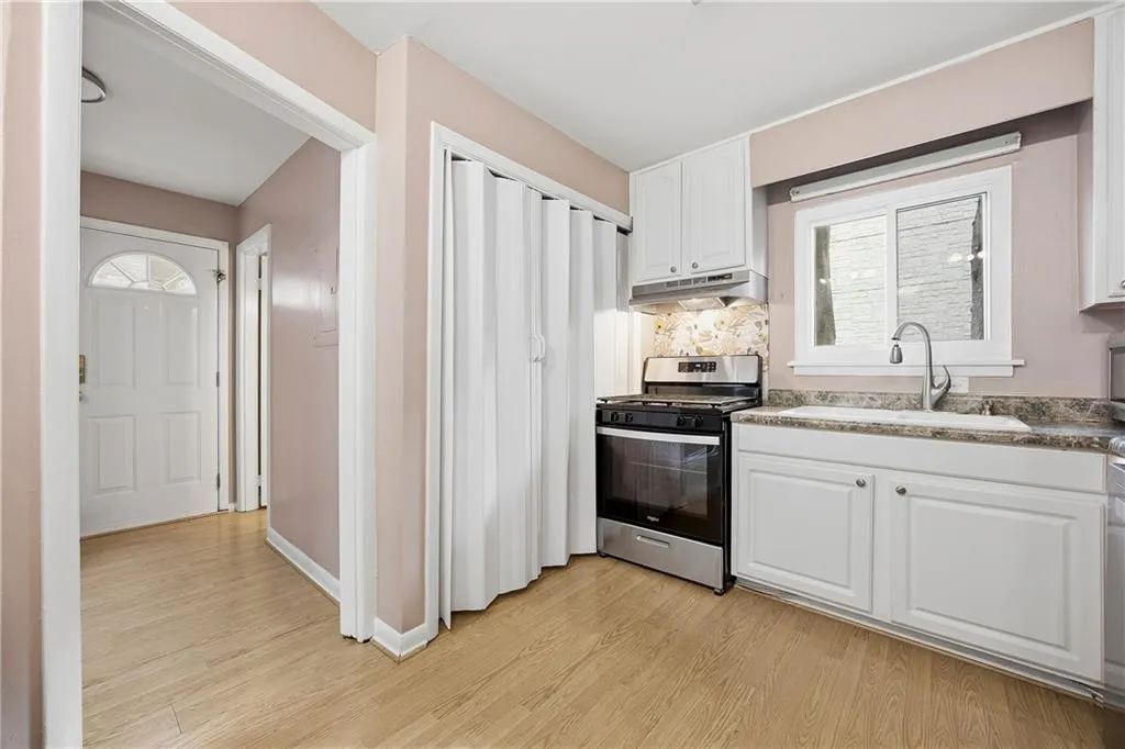 Kitchen featuring white cabinets, brand new stainless steel gas stove, light wood-style floors, under cabinet range hood, and backsplash