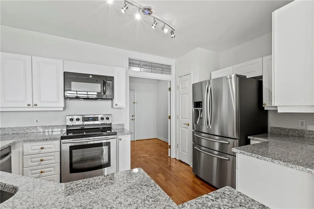 Kitchen featuring stainless steel appliances, white cabinetry, light stone counters, and track lighting